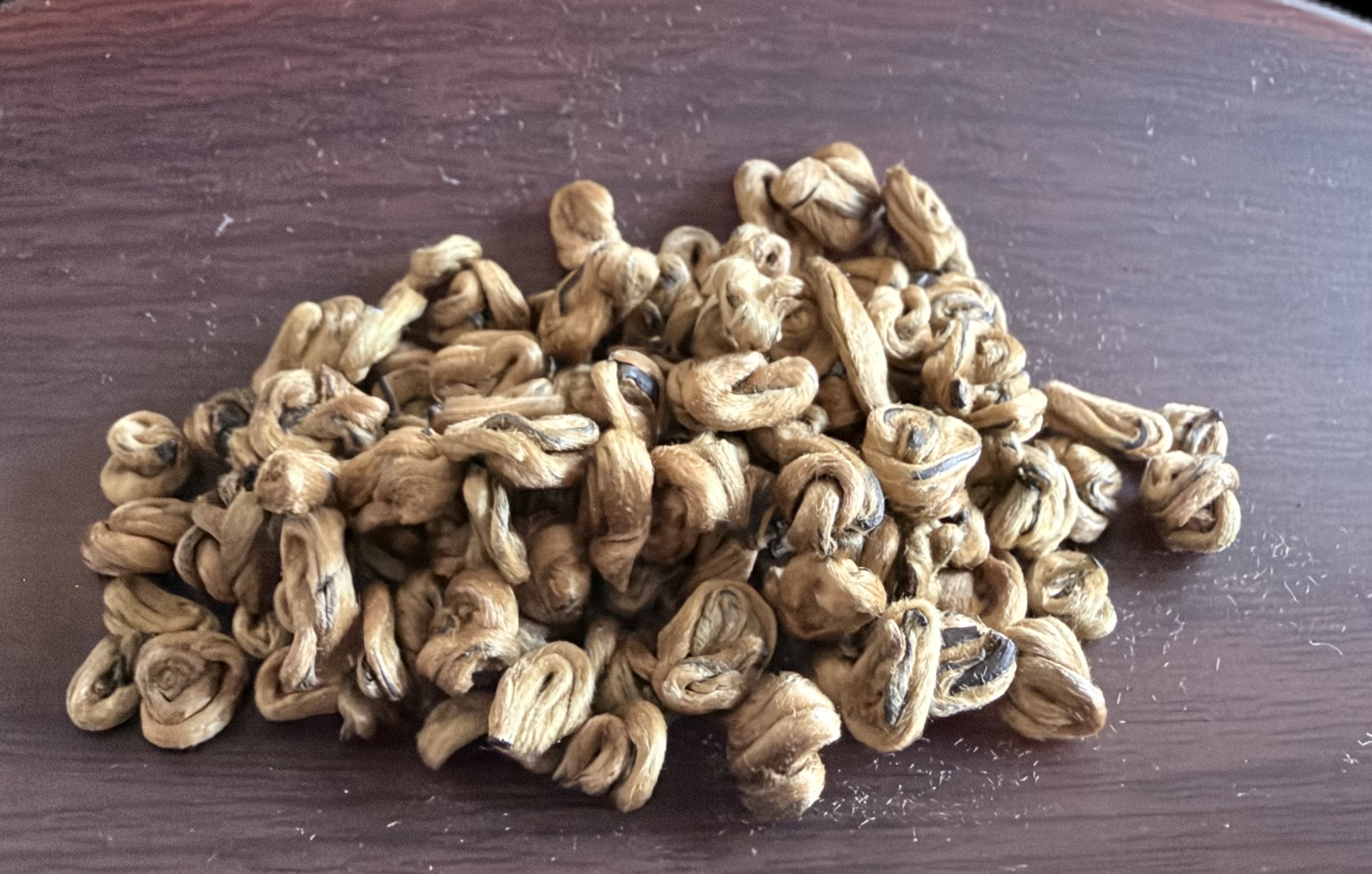 Tightly rolled dry Imperial Gold Bi Luo Chun black tea leaves on a wooden tray